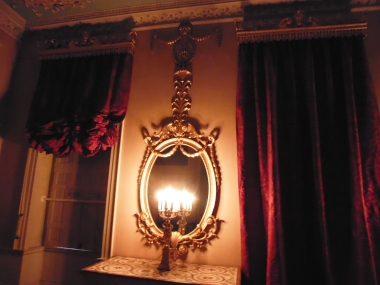 Two of the Eating Room's curtains, with one raised and other still lowered, as well as one of oval mirrors.